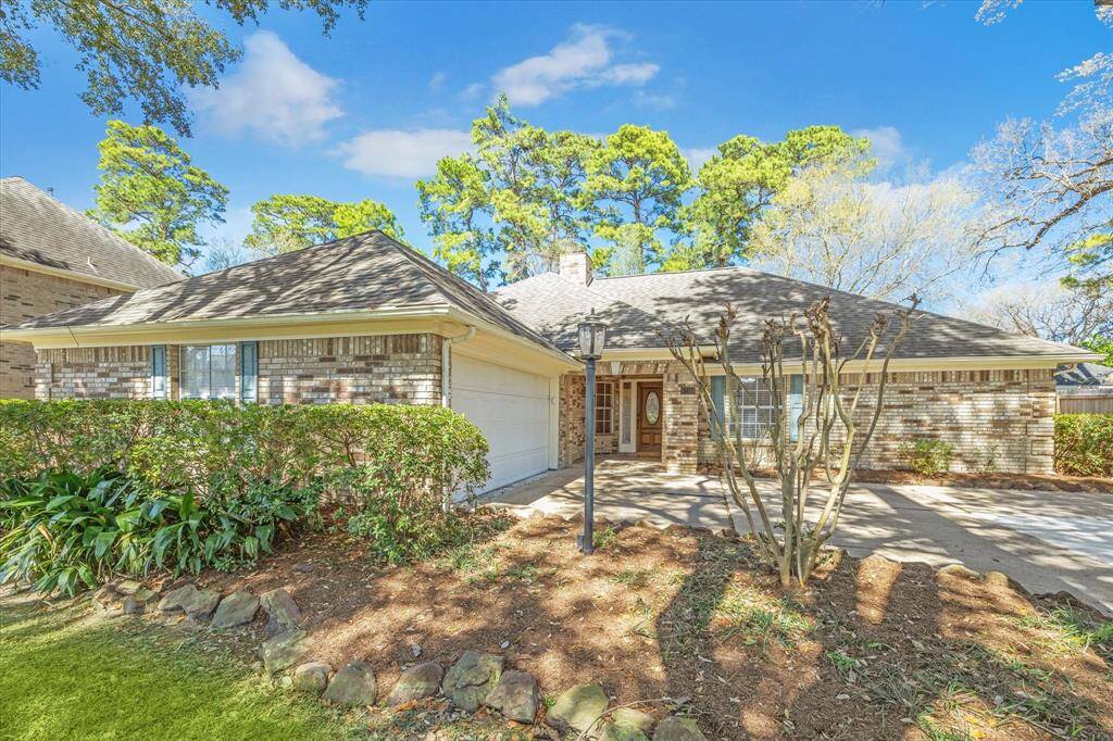 Charming single-story home with a brick exterior, featuring a two-car garage and a welcoming front entrance. The property is surrounded by mature trees and landscaped shrubs, offering a serene and inviting atmosphere.