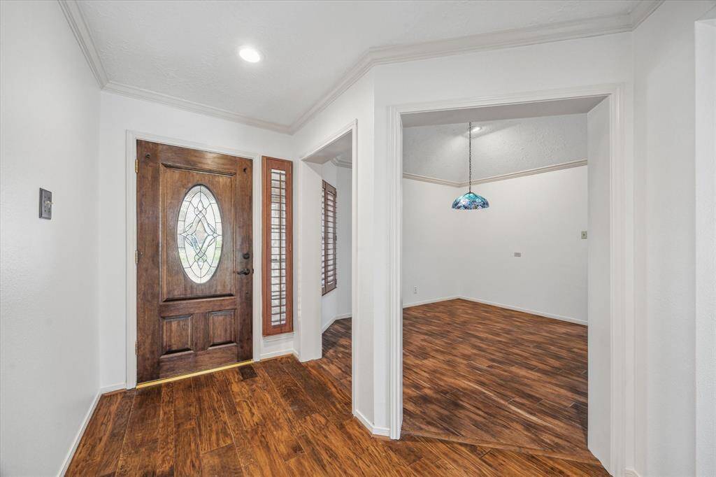This photo showcases a welcoming entryway with a wooden front door featuring an oval glass insert. To the left is an inviting dining room to share meals with loved ones.