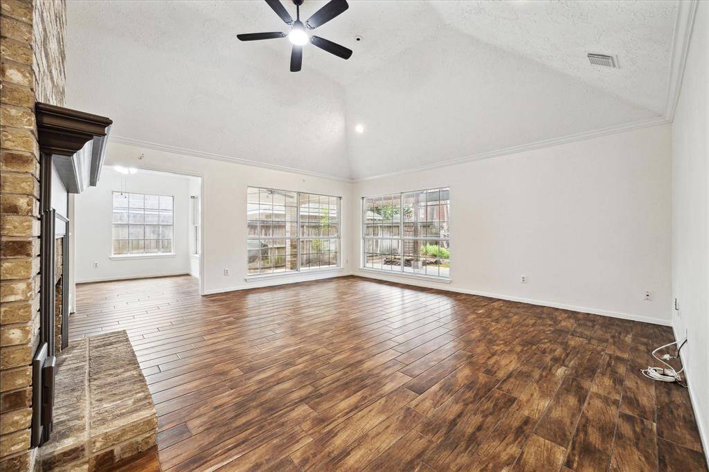 Bright and spacious primary room with newly carpeted flooring and a vaulted ceiling featuring a modern ceiling fan. Large windows with plantation shutters provide ample natural light. The room connects to a spacious bathroom, hallway and flex room, creating an open and airy feel.