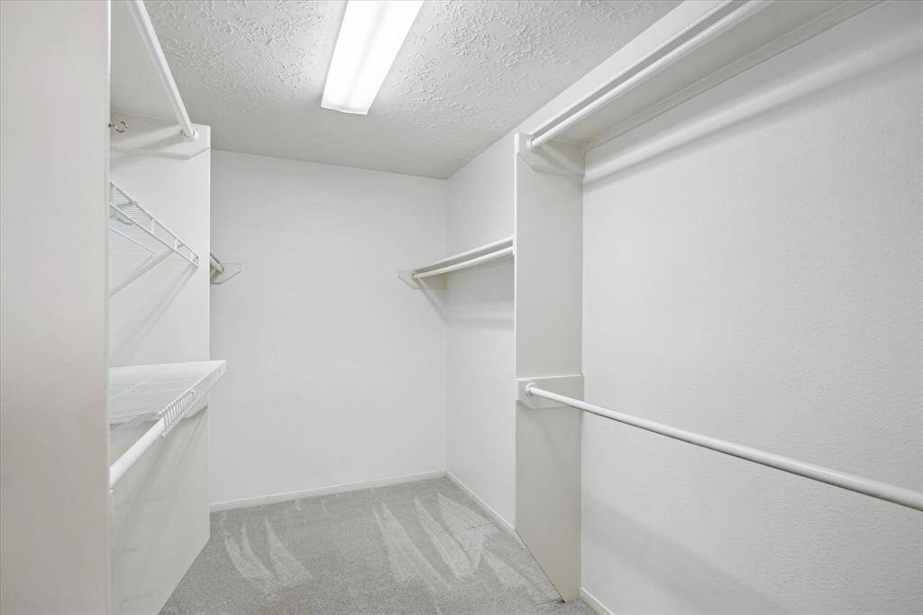 This spacious walk-in closet has ample shelving and hanging rods, featuring bright lighting and a clean, carpeted floor.