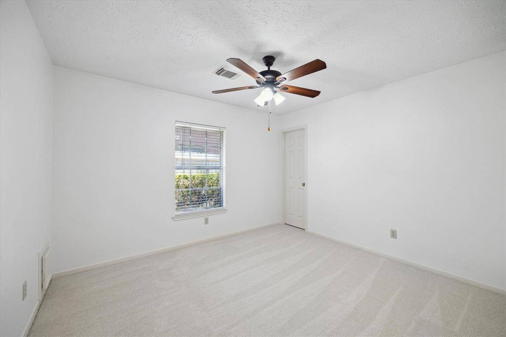 This secondary bedroom features freshly painted walls and new carpet, a lighted ceiling fan, and a window with blinds allowing natural light, creating a bright and airy space.