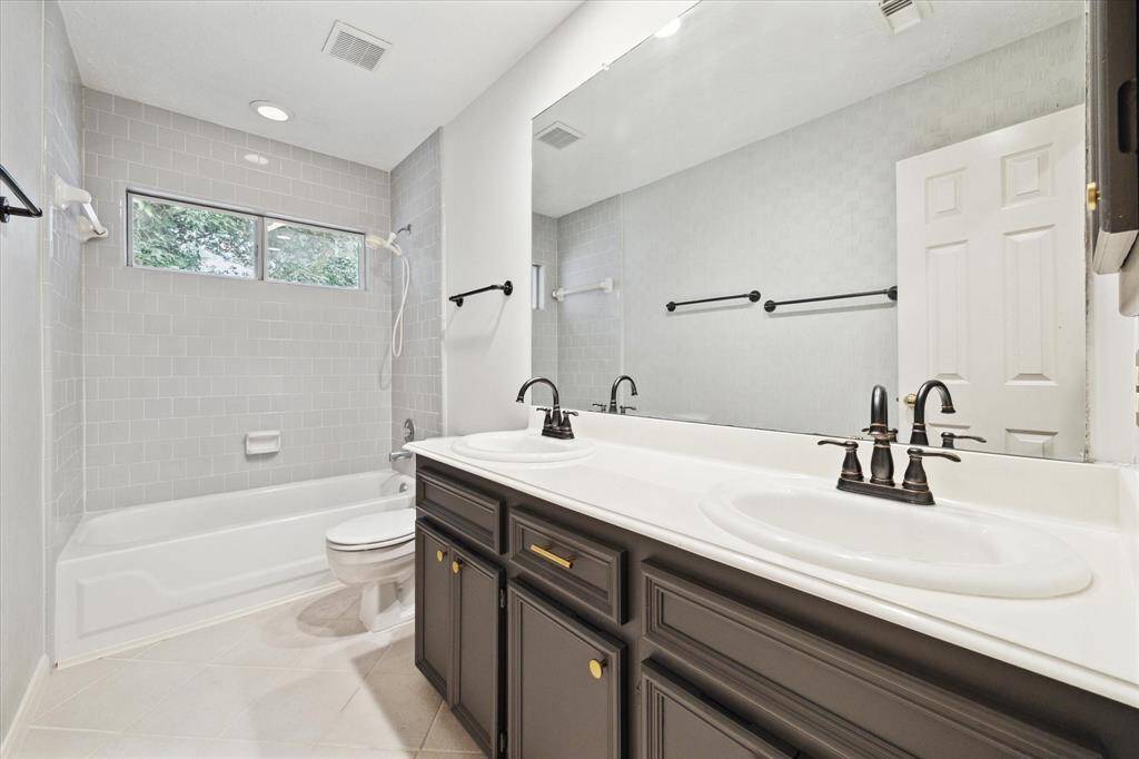 The guest bathroom features a double vanity with stylish fixtures, a large mirror, and a tiled bathtub . It offers a clean, bright space with ample lighting and storage beneath the sinks. Check out the freshly updated cabinetry.
