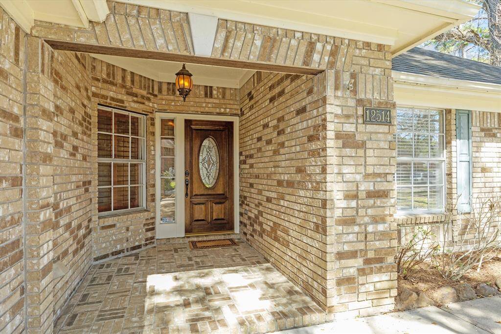 This welcoming entryway features a charming brick exterior, an elegant wooden front door with decorative glass, and a cozy porch with a warm hanging lantern.