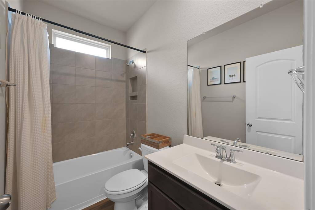 This is a modern, well-lit full bathroom with a tiled shower-tub combo, a single sink vanity with ample countertop space.