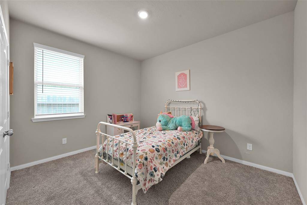 This is a cozy, well-lit bedroom featuring neutral walls and carpet flooring, with a single window providing natural light. Ideal for a child's room or guest space.
