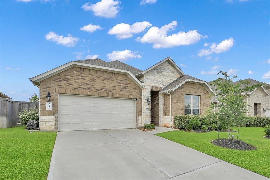 This is a single-story home featuring a brick facade with stone accents, a two-car garage, and manicured landscaping. It has a welcoming entryway and a well-maintained lawn, situated under the stunning Texas skies.