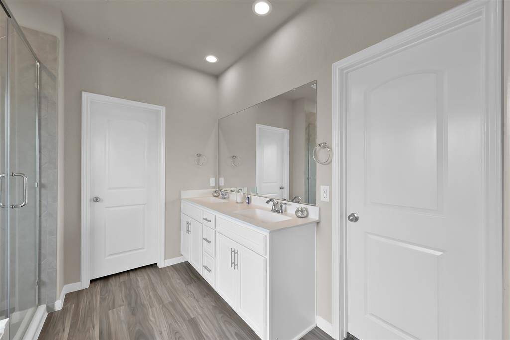 This is a modern bathroom featuring a double vanity with ample storage, a large mirror, sleek fixtures, and a glass-enclosed shower and separate soaking tub.