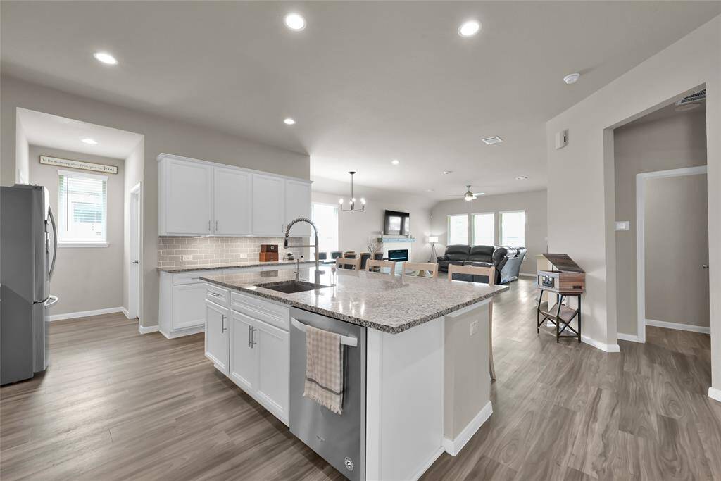 This is a modern, open-concept kitchen with white cabinetry, granite countertops, gas range, and stainless steel appliances. The layout flows seamlessly into the living area, offering a spacious feel, perfect for entertaining or family living. The room features recessed lighting and wood-like flooring throughout.