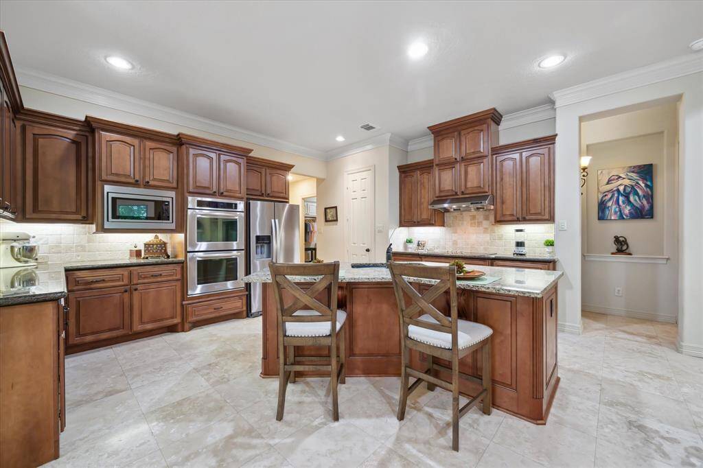 Kitchen is equipped with double ovens, undermount lighting, granite countertops, and abundant custom cabinetry for ample storage.