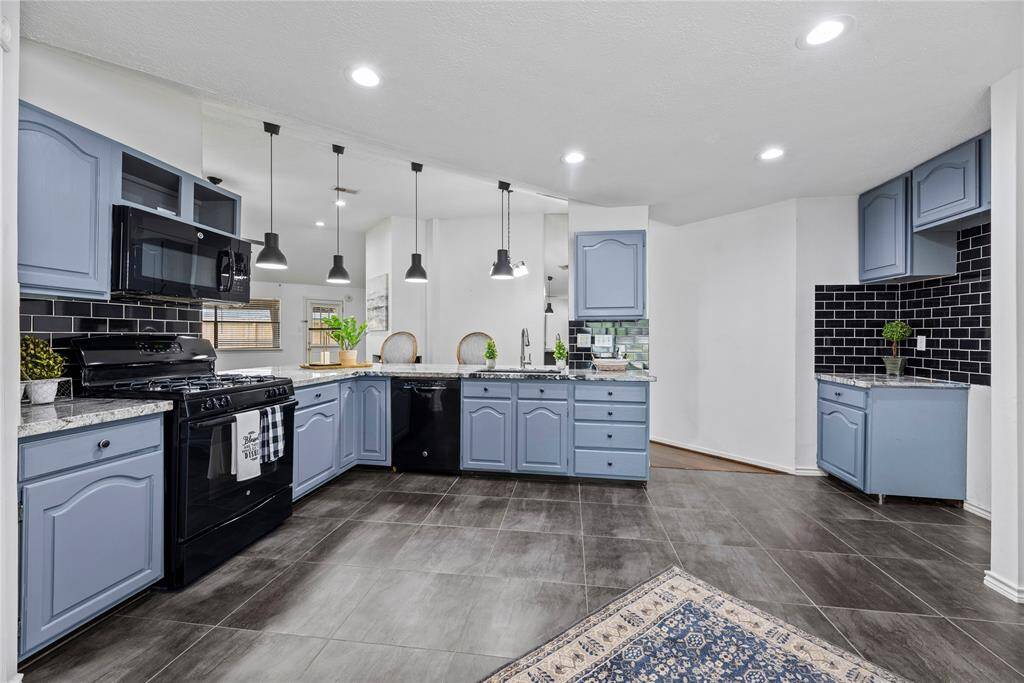 This modern kitchen features a stylish bar with granite countertops, elegant pendant lighting, and cozy seating. The open layout includes built-in shelving, dark wood floors, and sleek cabinetry with a contrasting black tile backsplash, creating a sophisticated and inviting space.