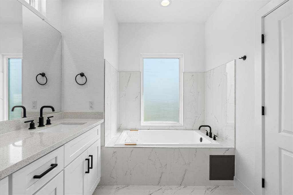 The primary bathroom is a luxurious retreat, featuring dual vanity sinks with ample storage, a private water closet, a beautifully tiled standing shower with a frameless glass door, and a soaking tub elegantly encased in matching tile. Stunning lighting throughout completes this serene space!