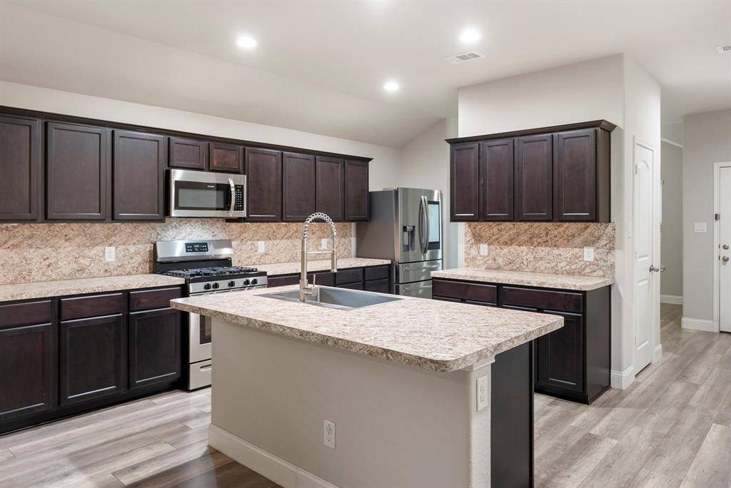 This modern kitchen features including a gas stove and microwave. The open layout provides ample space, with breakfast bar and contemporary lighting.