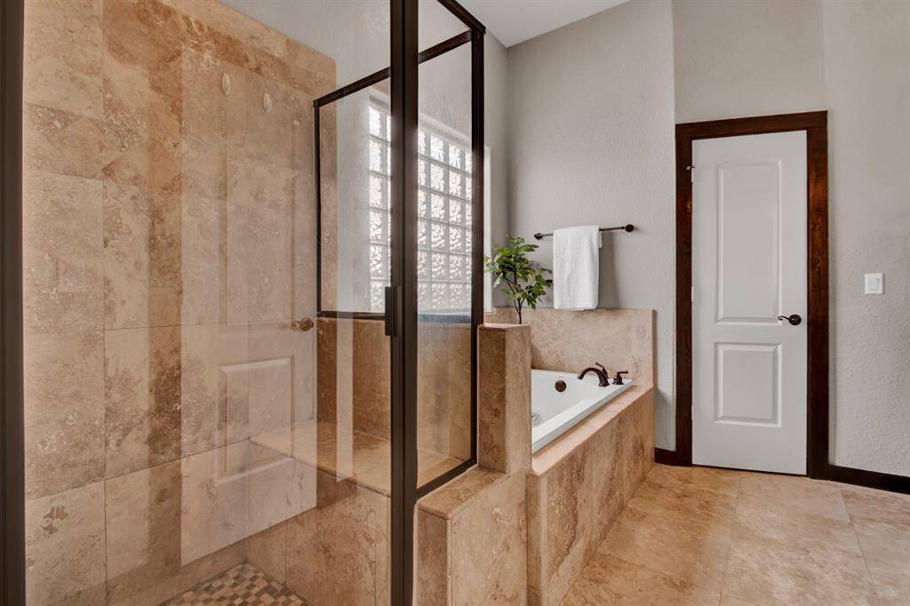 A walk-in shower with built-in bench and large jetted tub are framed by stone finishes, blending functionality with spa-like comfort.