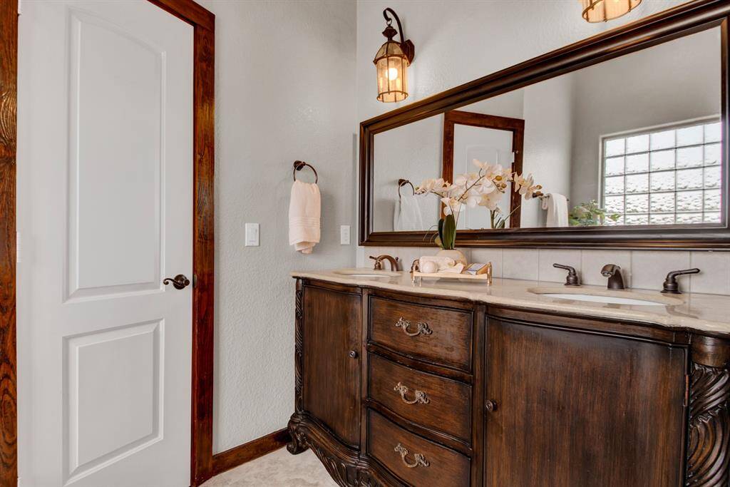 The primary bathroom showcases a dual-sink vanity with carved wood detail, coordinating bronze fixtures, an oversized mirror, and a secondary primary walk-in closet.