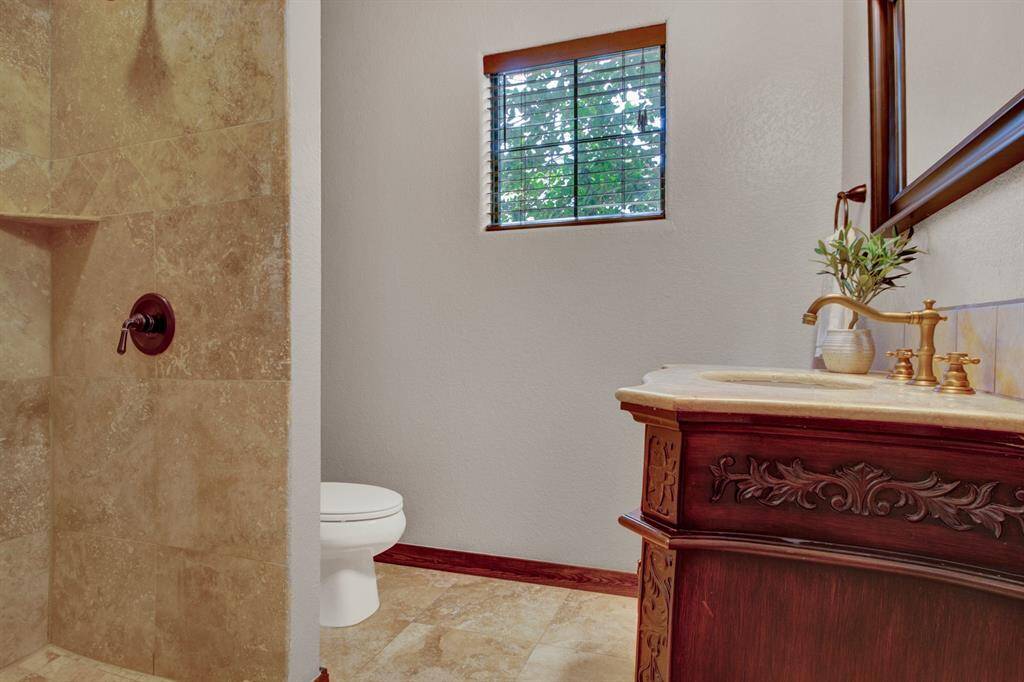 The first-floor bath features travertine tile, a walk-in shower, and a richly detailed vanity with brass fixtures, blending charm and functionality.