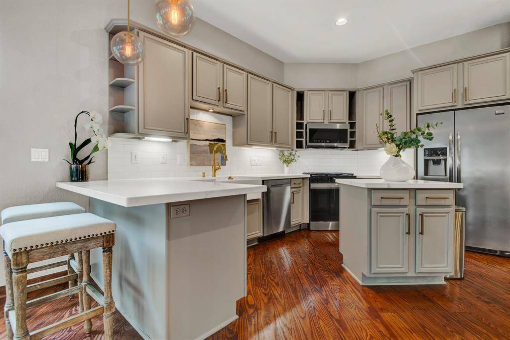 The modern kitchen is equipped with quartz countertops, a center island, custom cabinetry, and stainless steel appliances - accented by chic pendant lighting. ALL appliances included in the sale.