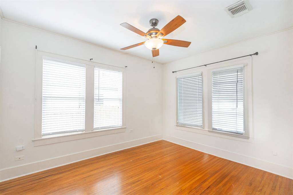 This bright, airy, primary bedroom features hardwood flooring, large windows, and a ceiling fan, creating a comfortable and inviting space.