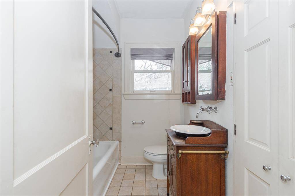 This bathroom features a vintage-style vanity with a modern vessel sink, tiled walls surrounding the bathtub, and a window for natural light. It combines classic charm with functionality.