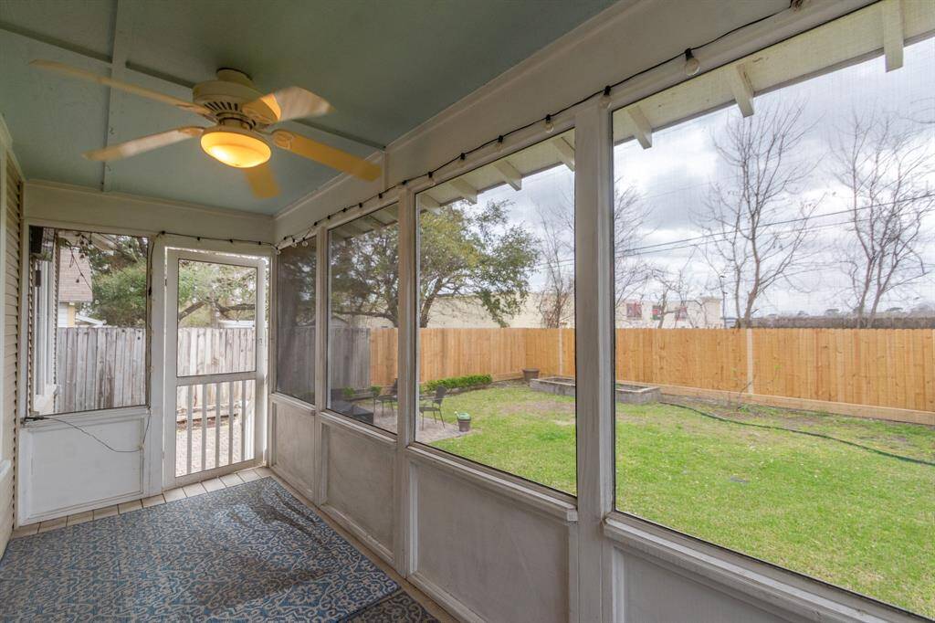 A cozy screened-in porch with a ceiling fan, overlooking a fenced backyard with a lawn and trees, offering a peaceful outdoor space.