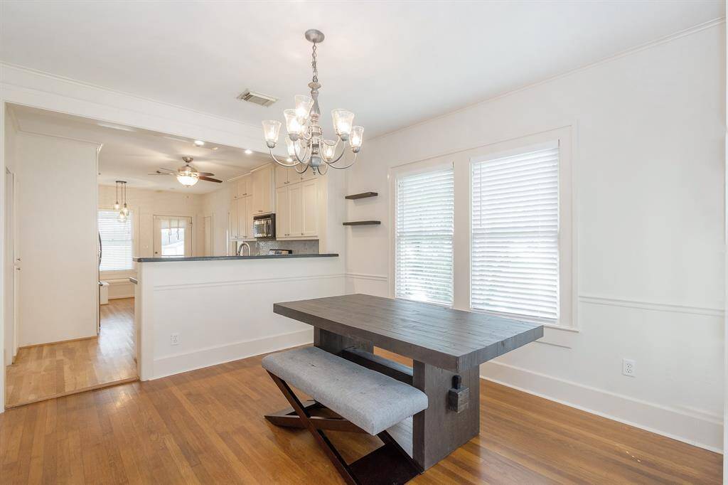 Bright dining area with hardwood floors, featuring a modern chandelier and a window with blinds.