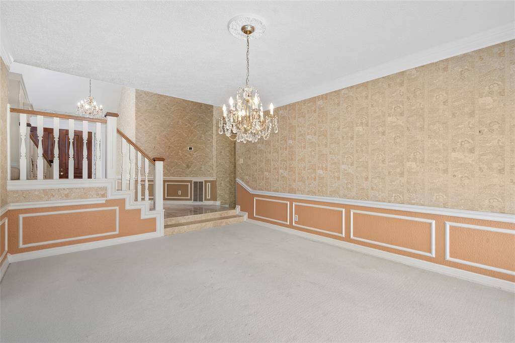 Another view of your dining room showing two vintage chandeliers and decorative wall paneling. The split-level design with carpeted flooring adds charm and character.