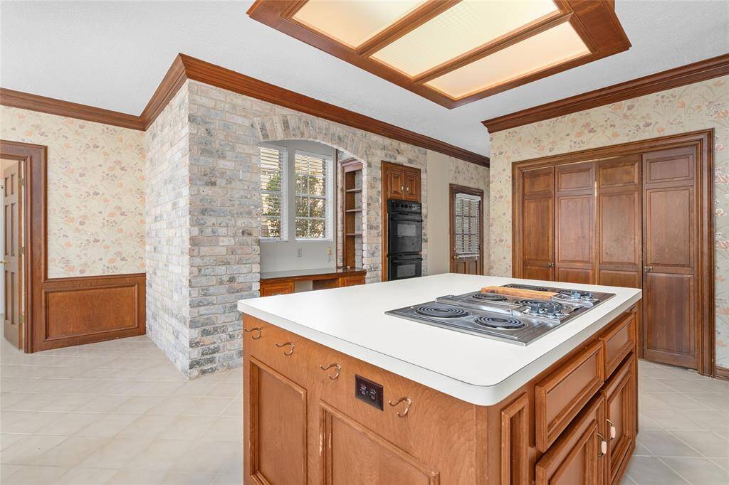 From this view of your kitchen, you get a better look at the island with a built-in cooktop surrounded by warm wood cabinetry. The unique brick archway houses a desk with shelving and ample storage. The double oven offers both style and functionality.