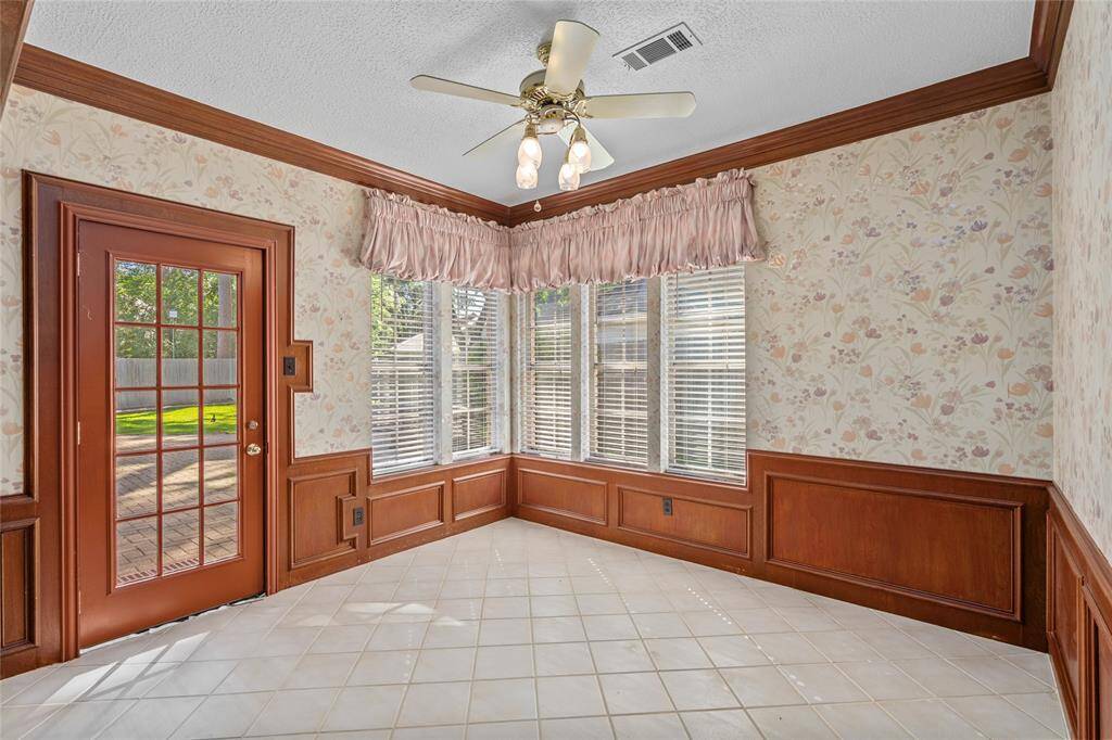 Your bright breakfast nook has large windows, a ceiling fan, wood wainscoting with matching crown molding and tile flooring with a view of the backyard through a glass door.