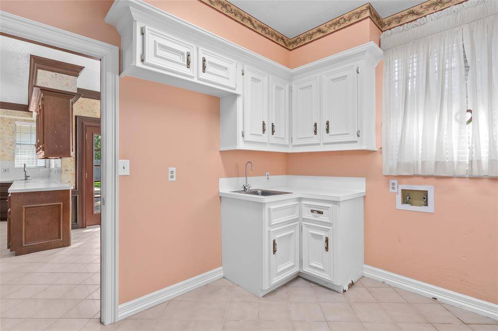 Your new laundry room has white cabinetry, tile flooring, a sink and is adjacent to the kitchen. The window allows ample natural lighting.
