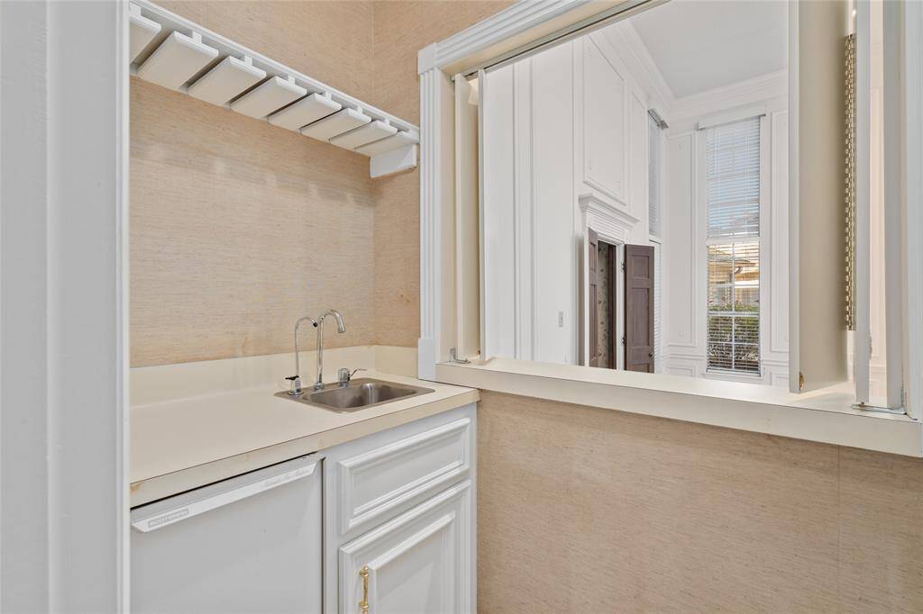 Your downstairs wet bar area contains a small sink, white cabinetry, ice machine and shelving with a wine glass rack. A window with decorative trim opens into the living room enhancing the space with natural light.