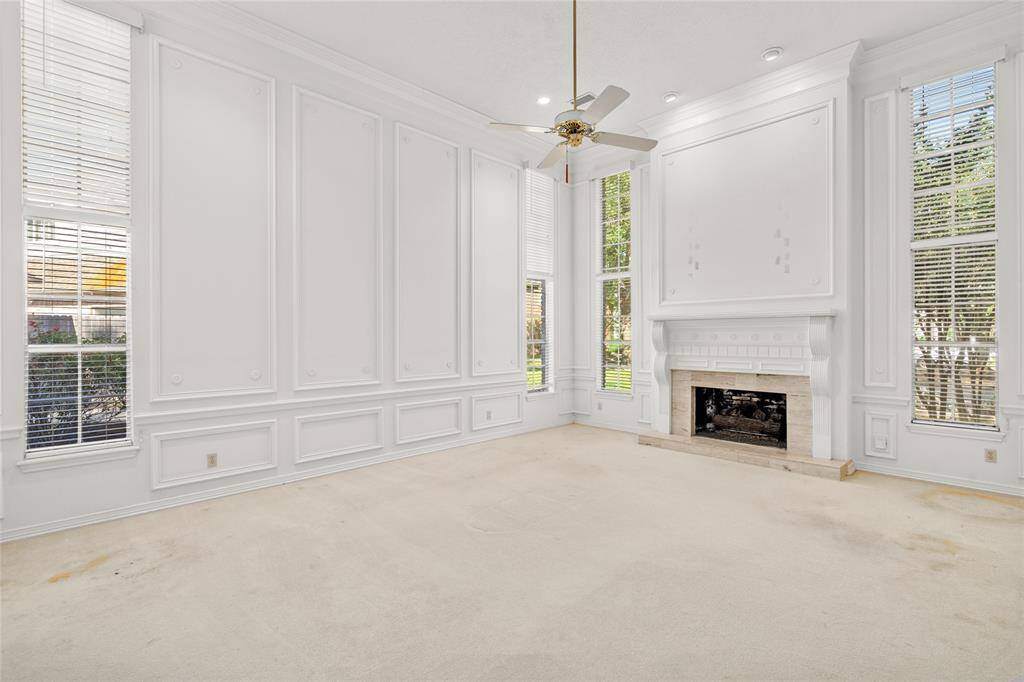 Your enormous  living room features high ceilings, crown molding, elegant wall paneling, a large fireplace and abundant natural light streaming through tall windows.