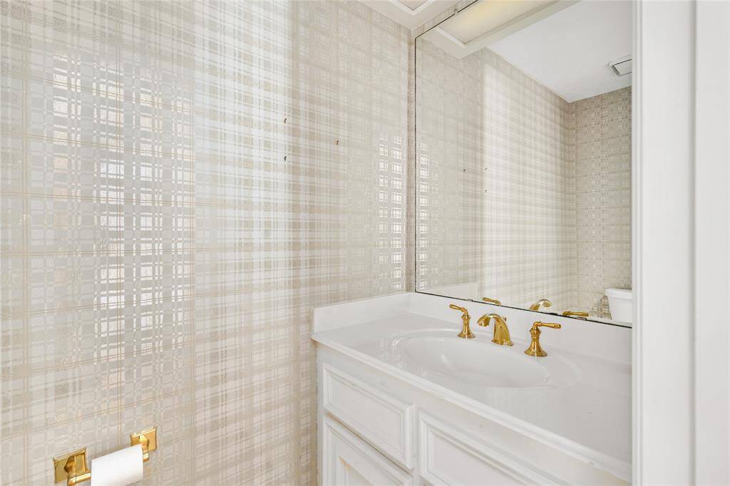 Your cozy downstairs half bath has elegant gold fixtures, a large mirror, and stylish patterned wallpaper creating a bright and inviting space.