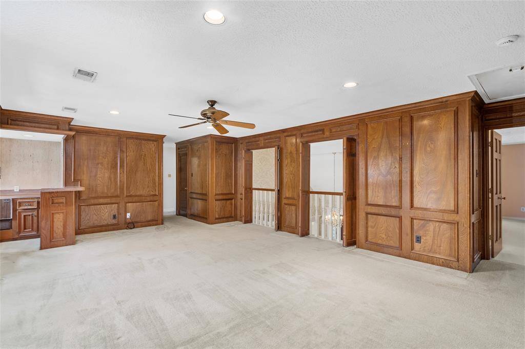 This spacious room features elegant wood paneling, a ceiling fan, and built-in shelving. It offers a cozy yet open atmosphere, perfect for a living area or home office.