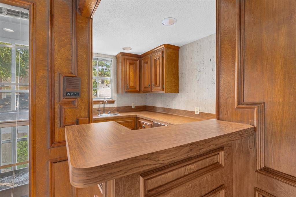 This photo showcases a cozy kitchen with warm wood cabinetry and paneling, featuring a small breakfast bar. Natural light streams in through a window above the sink, creating a bright and inviting atmosphere.