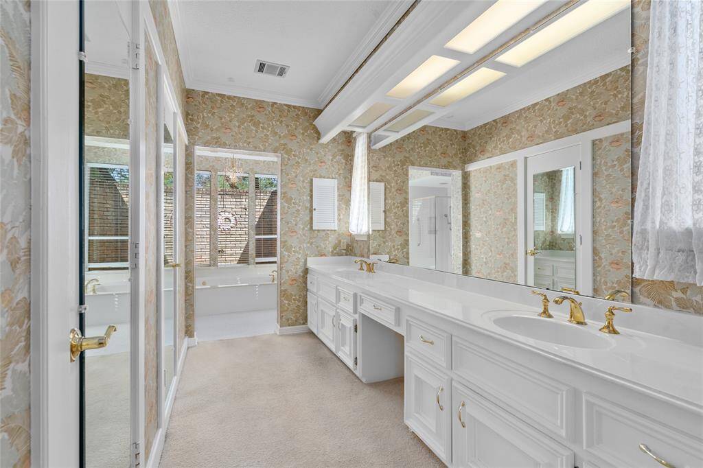 Your expansive primary bath boasts double sinks with gold fixtures, white cabinets, a vanity, and ample natural light from large windows. Enjoy a relaxing soak in your soaking bathtub with jets. Your new primary bath also has a separate glass-enclosed shower.