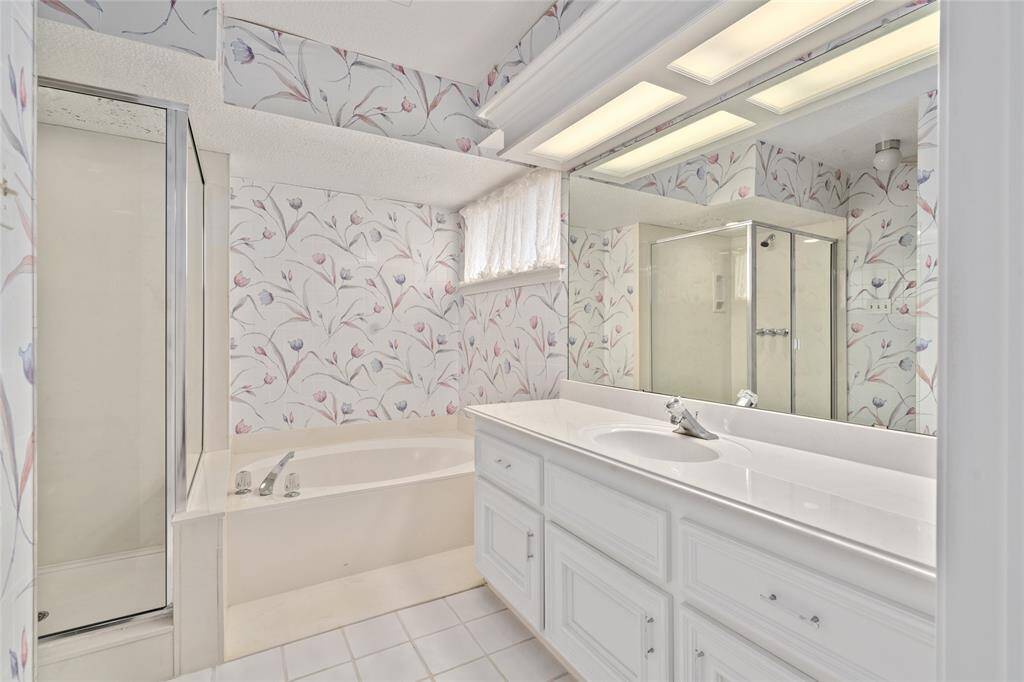 This en-suite bath features extra long sink vanity and separate shower and soaking bathtub. The space is bright and airy with ample lighting and a large mirror.