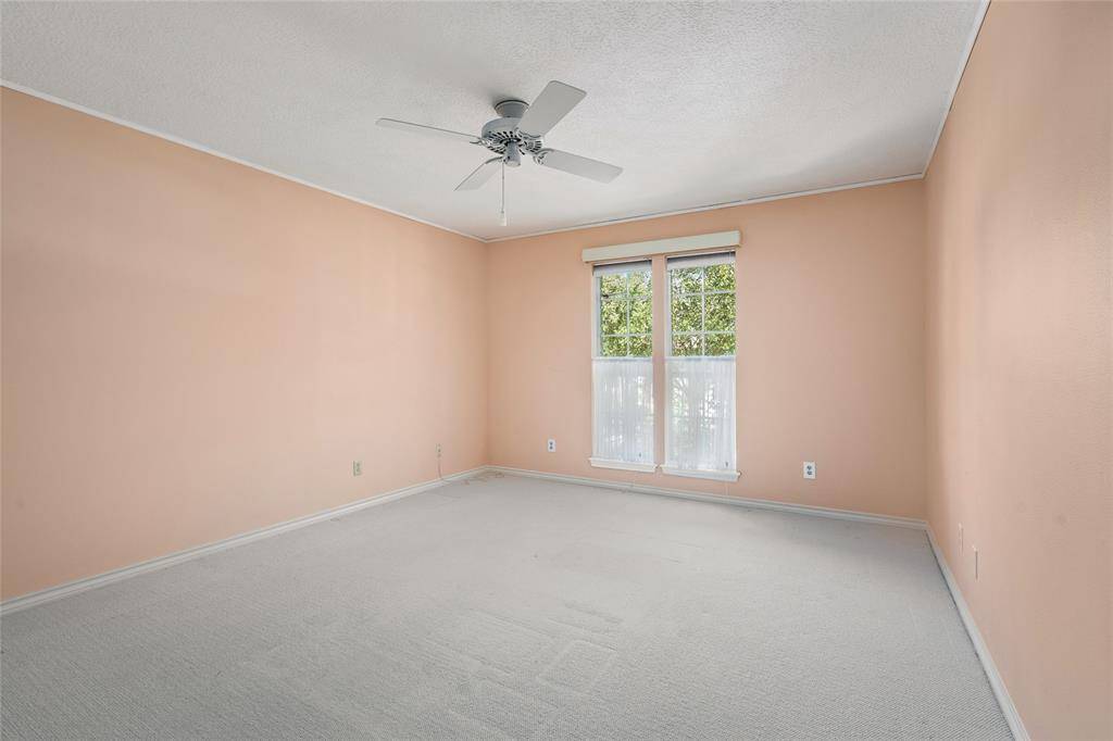 Another upstairs bedroom with crown molding, carpet, and a ceiling fan. The window, provides natural light and a view of the surrounding trees.