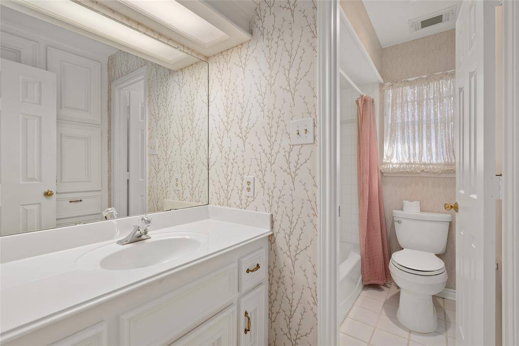 This en-suite bath has a clean design with a white vanity and large mirror with a bathtub and shower combo and a window for natural light.