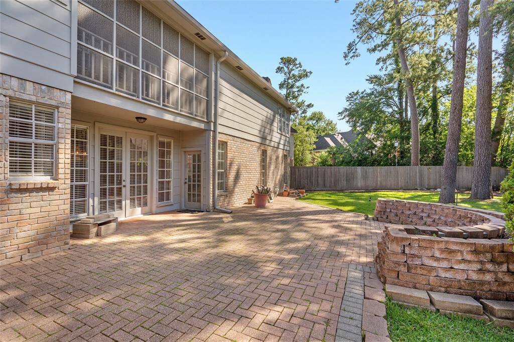Another view of your backyard with a large brick patio and brick walled garden making this the perfect place for outdoor entertaining. The area is surrounded by mature trees and a wooden fence. The back of the house features large windows and French doors.
