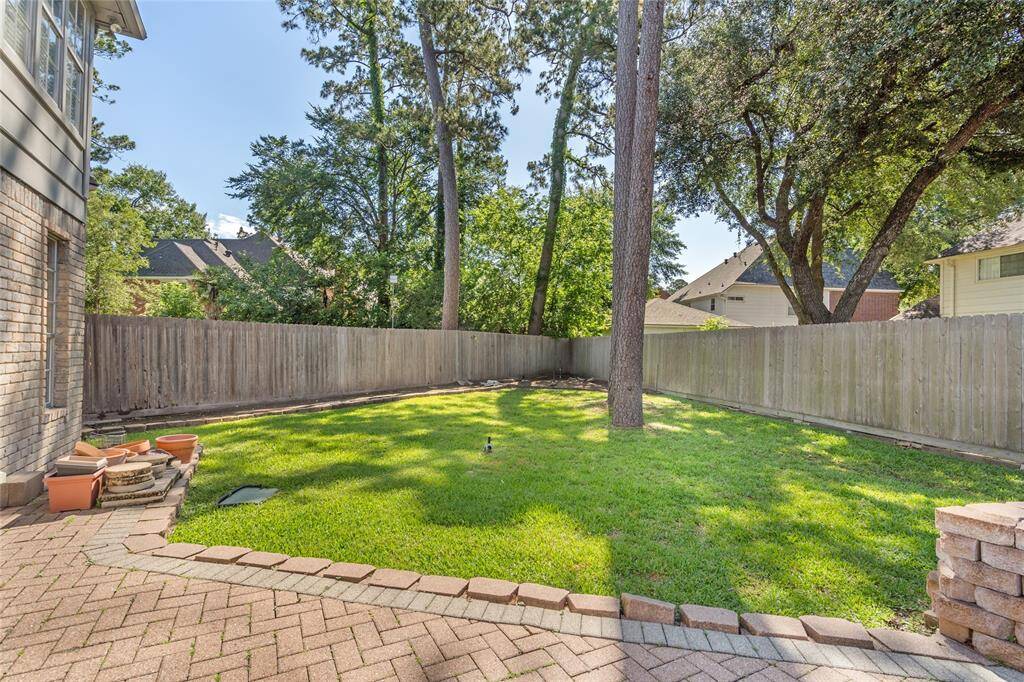 Your new back yard is surrounded by a wooden fence for privacy. Tall trees provide shade, and a paved patio area is ideal for outdoor activities or relaxing.