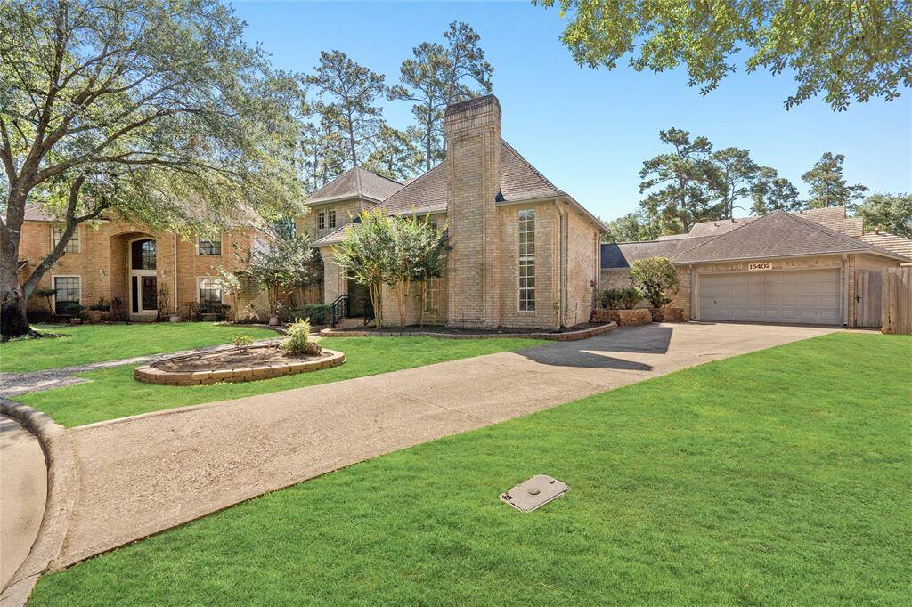 Another view of your spacious two-story brick home mature trees and a circular flower bed. The house is set in a serene neighborhood with tall trees in the background.