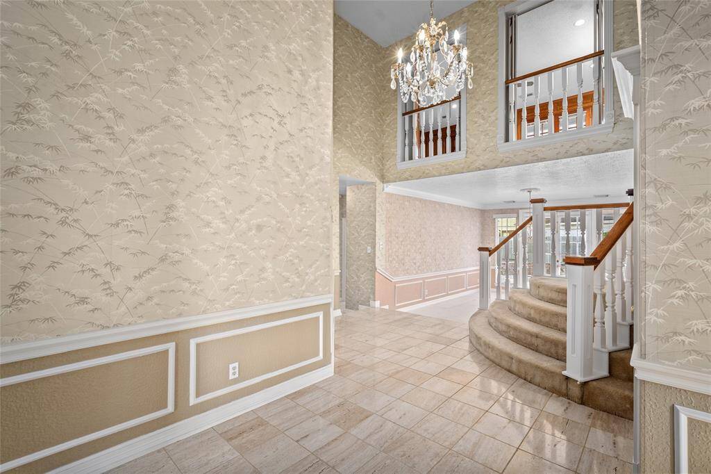Another view of your foyer features the  grand staircase, chandelier, and wainscoting. The open layout includes tile flooring and a view of the upper level.