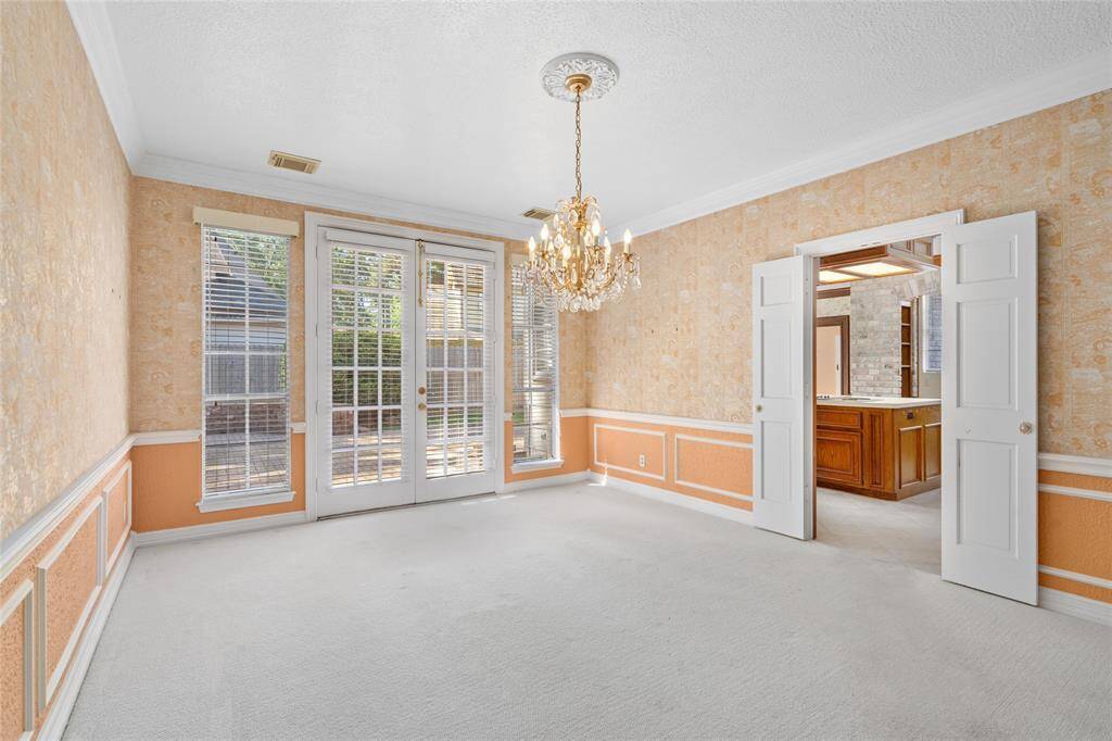 Your formal dining room features a classic chandelier, French doors leading to a patio, crown molding, and wainscoting. Ample natural light enhances the warm atmosphere.