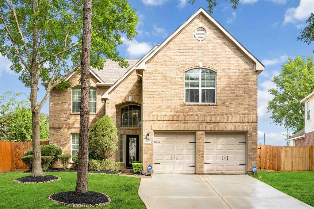 This is a charming two-story brick home featuring a double garage, well-maintained landscaping, and a welcoming front entrance. The lush green lawn and mature trees add to its curb appeal, creating an inviting atmosphere.