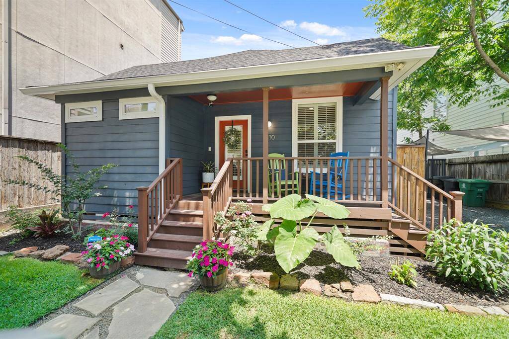 Charming 1920s Bungalow with a cozy front porch, featuring fresh blue siding and white trim. The inviting entrance is accented by colorful plants and a well-maintained lawn, perfect for relaxing.