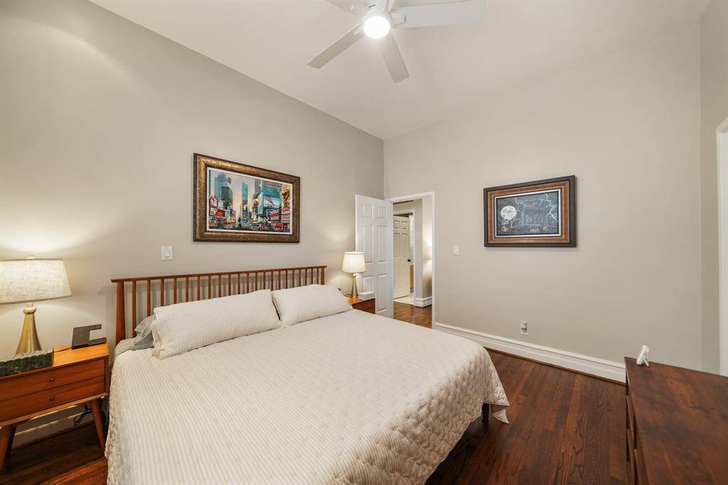 Another view of the cozy bedroom features warm hardwood floors, a cozy bed, and a ceiling fan. It includes a window with shutters for natural light, creating a serene and inviting atmosphere.