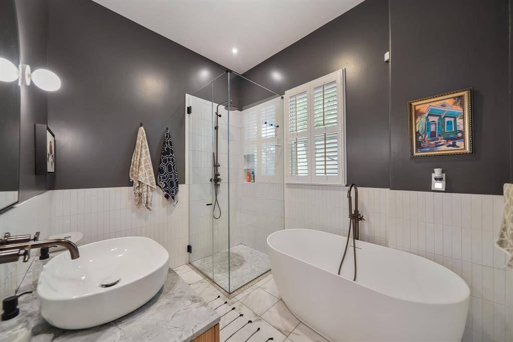 This modern bathroom features a sleek design with a freestanding bathtub and a spacious glass-enclosed shower. It has stylish dark walls, a unique vessel sink, and a marble countertop, creating a luxurious and inviting atmosphere.