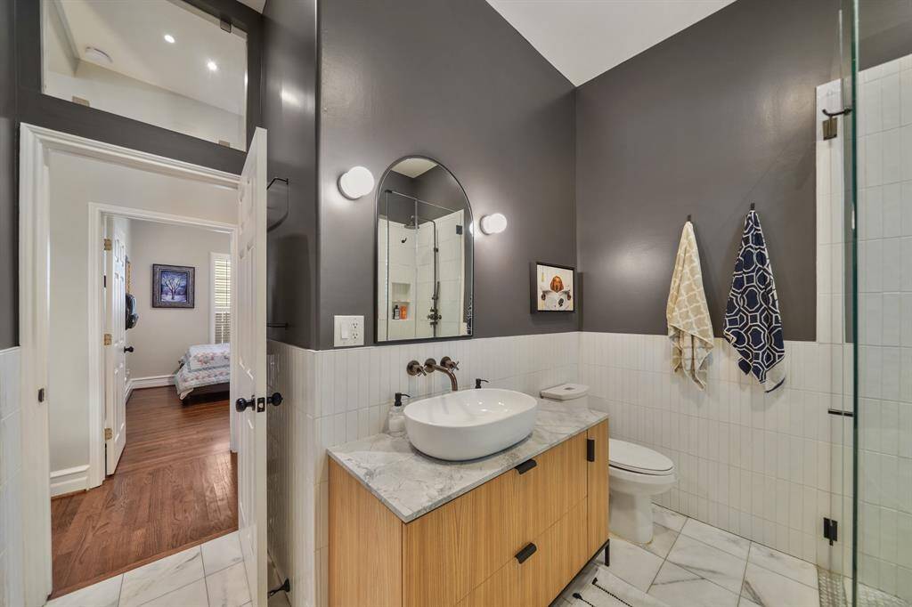This photo showcases a modern bathroom with stylish dark walls and a white tile wainscot. It features a sleek vanity with a vessel sink, a large mirror, and contemporary lighting.