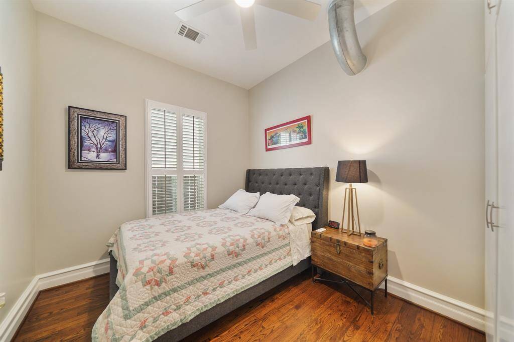 Cozy bedroom with hardwood floors, featuring a ceiling fan and has a window with shutters for natural light.