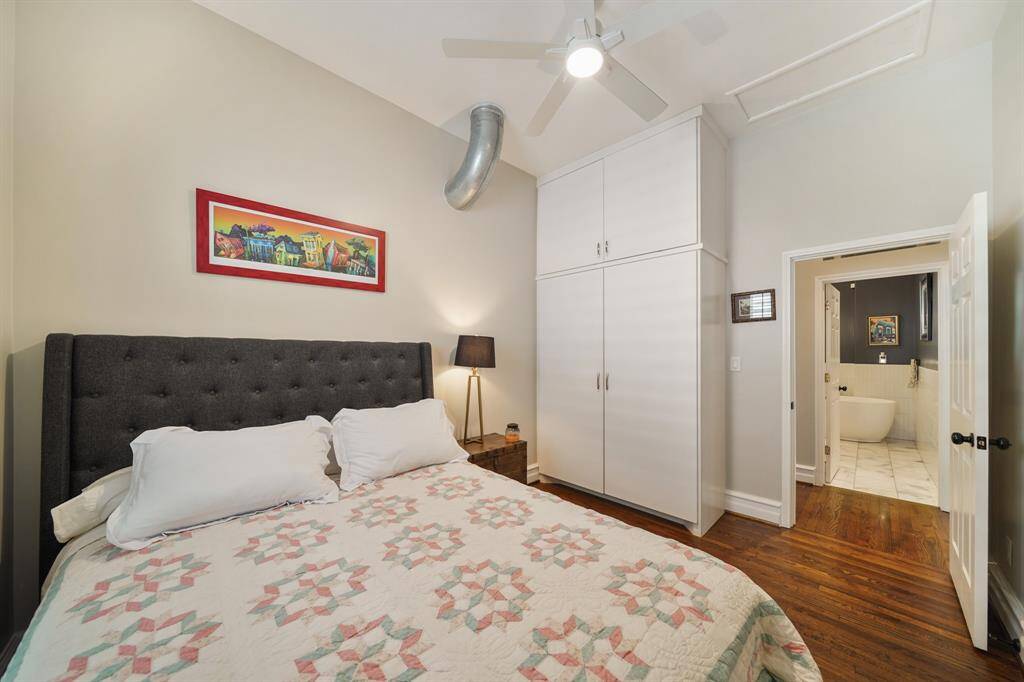 Here's a another angle of the bedroom with hardwood floors, featuring a ceiling fan and has a window with shutters for natural light.