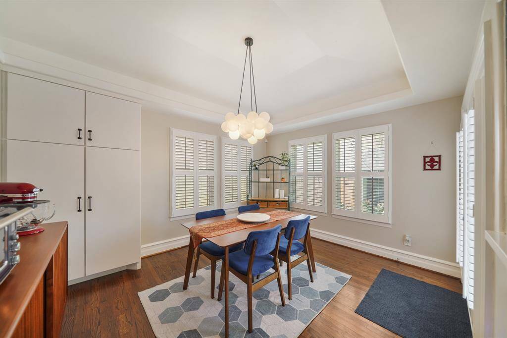 Bright and inviting dining area with hardwood floors, featuring a modern light fixture. The room has large windows with shutters perfect for meals and entertaining.